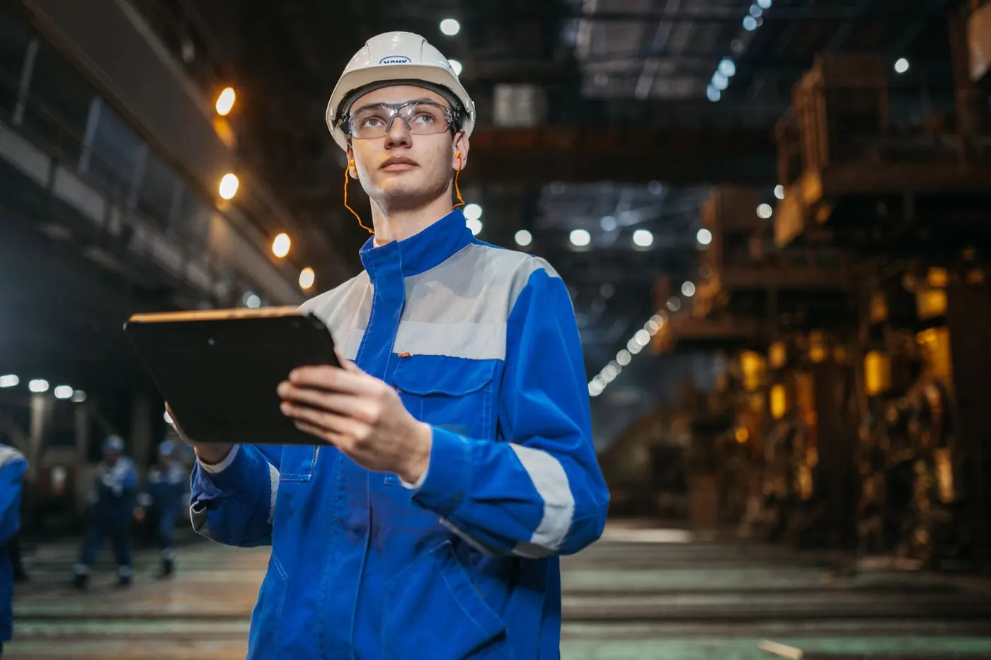 An engineer in safety gear with a tablet on a factory floor