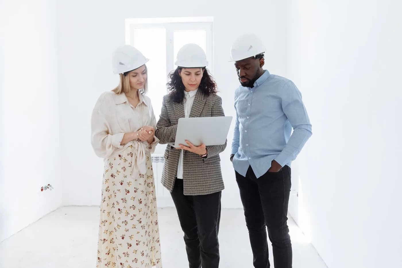 Three professionals in hard hats going through plans on a laptop